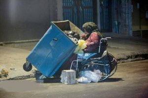 بانویی با ویلچر که به دنبال غذا در سطل زباله‌ها
